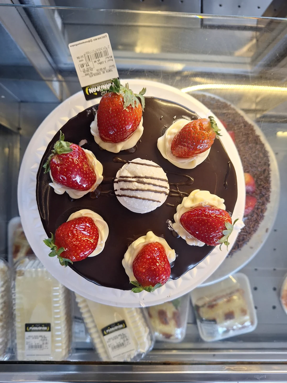Torta de chocolate da ManáPan com cobertura espelhada, morangos e suspiro, vista de cima na vitrine