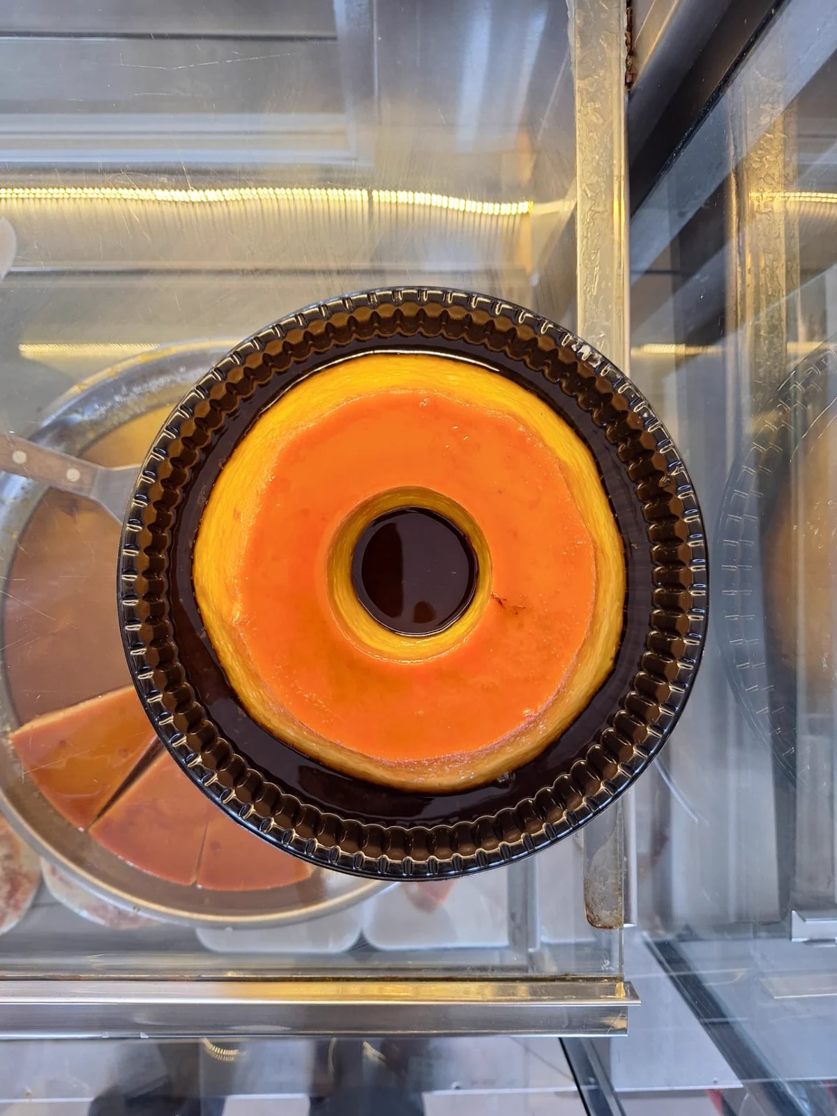 Pudim de leite condensado da ManáPan com calda de caramelo dourada em forma de pudim na vitrine refrigerada
